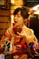 A woman in a kimono eating food with chopsticks.