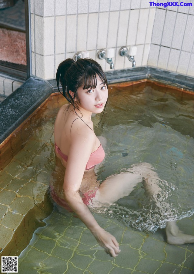 A woman in a pink bikini sitting in a bathtub.