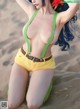 A woman with blue hair wearing yellow shorts and green suspenders.